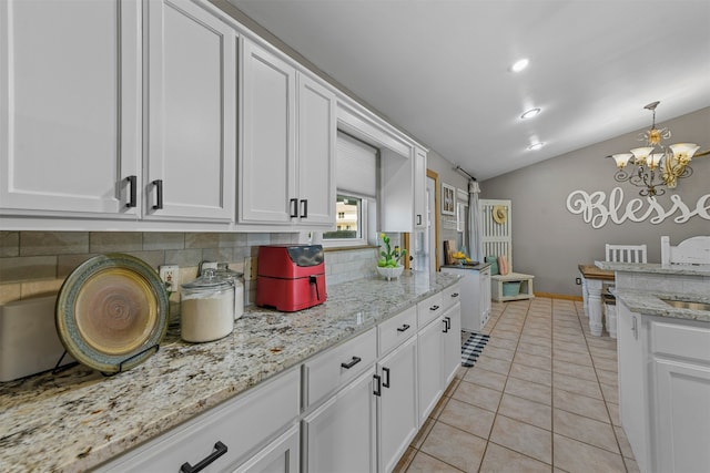 kitchen with decorative backsplash, a notable chandelier, white cabinetry, and vaulted ceiling