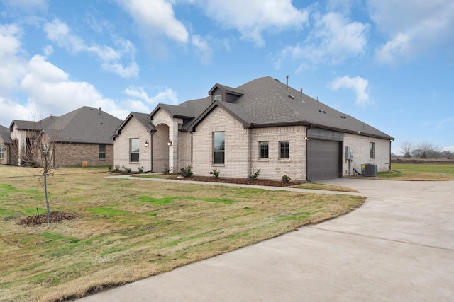 french provincial home with a front yard, central AC unit, and a garage