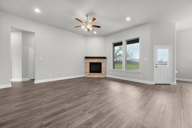 unfurnished living room with ceiling fan, dark wood-type flooring, and a brick fireplace