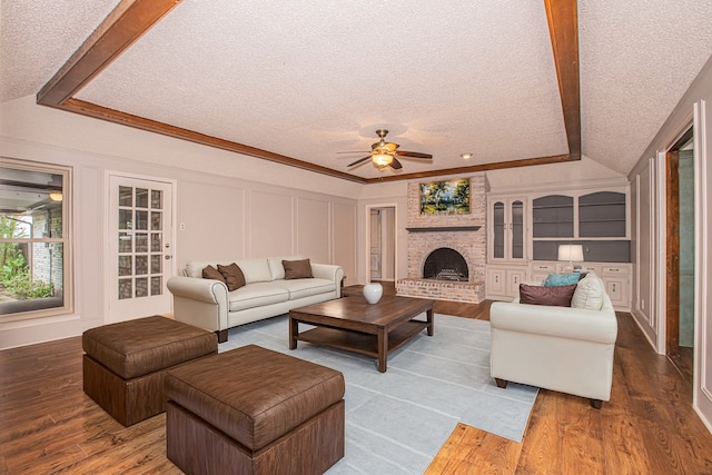 living room featuring ceiling fan, a fireplace, ornamental molding, hardwood / wood-style flooring, and a textured ceiling