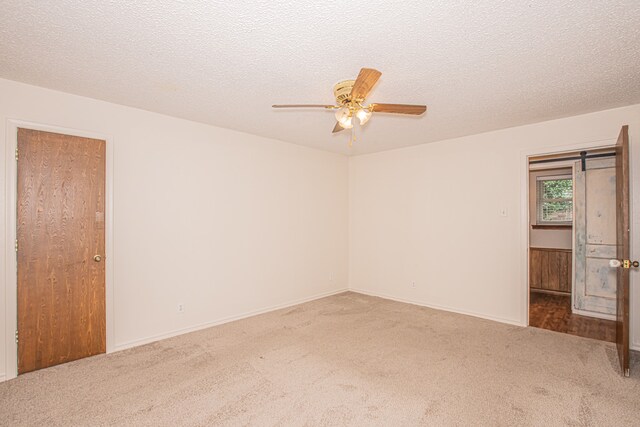 carpeted spare room featuring ceiling fan, a textured ceiling, and a barn door