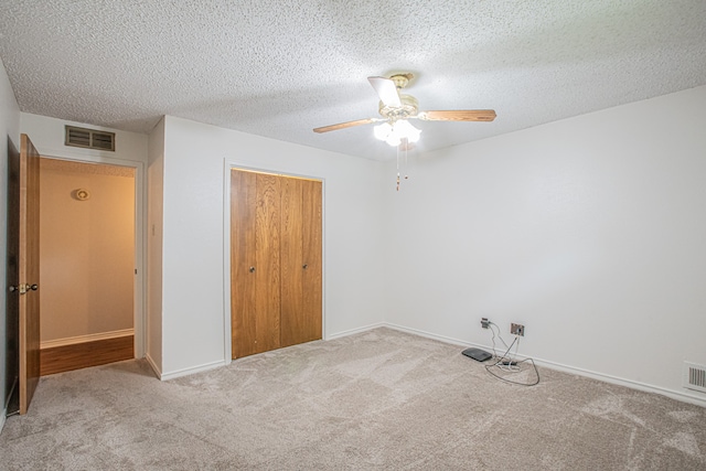 unfurnished bedroom with ceiling fan, a textured ceiling, a closet, and light carpet