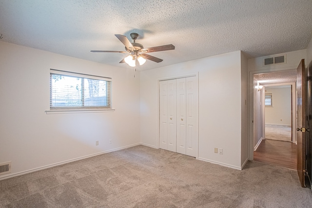 unfurnished bedroom with a textured ceiling, ceiling fan, a closet, and light colored carpet