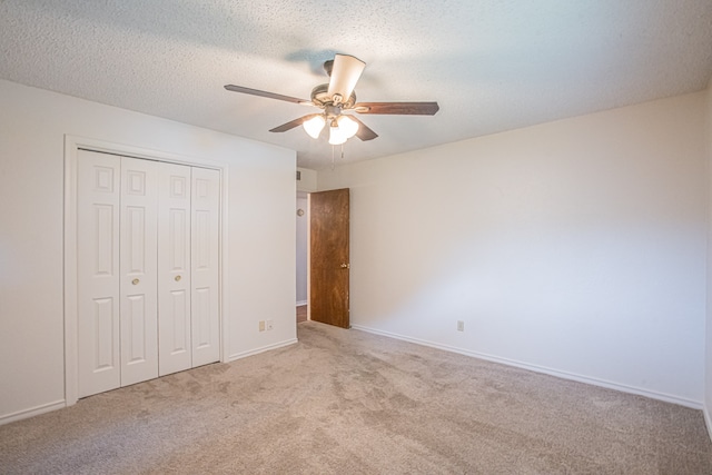 unfurnished bedroom featuring ceiling fan, a textured ceiling, a closet, and light carpet