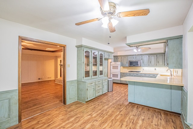 kitchen featuring stainless steel microwave, kitchen peninsula, light hardwood / wood-style flooring, and sink