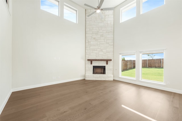 unfurnished living room featuring a fireplace, wood-type flooring, a towering ceiling, and ceiling fan