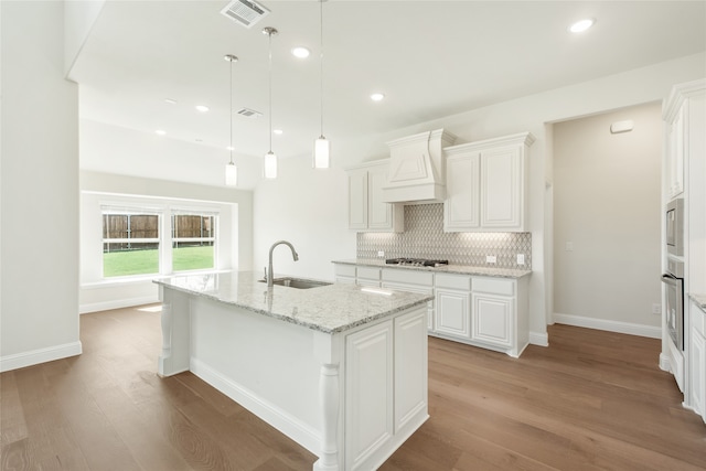 kitchen with white cabinetry, pendant lighting, light hardwood / wood-style flooring, premium range hood, and a center island with sink