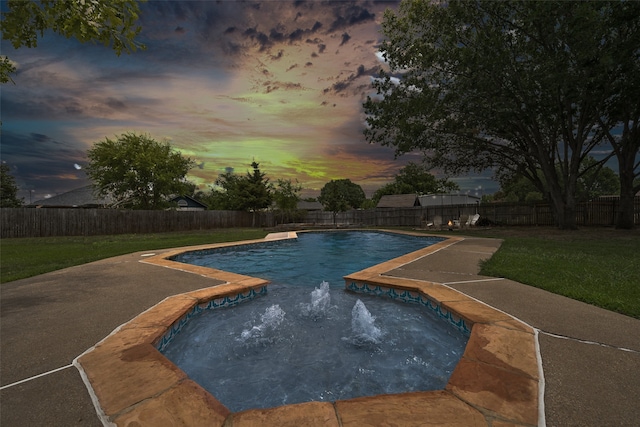 pool at dusk with a yard, a jacuzzi, and pool water feature