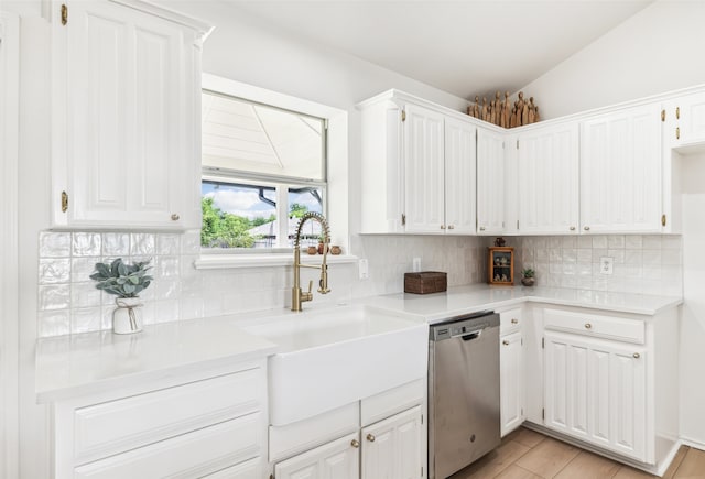 kitchen with stainless steel dishwasher, vaulted ceiling, sink, and white cabinets