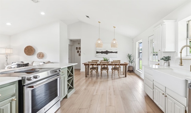 kitchen with white cabinets, light hardwood / wood-style flooring, stainless steel appliances, lofted ceiling, and pendant lighting