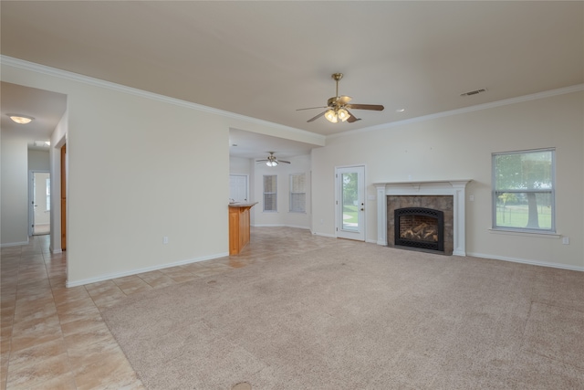 unfurnished living room featuring a tile fireplace, crown molding, ceiling fan, and light colored carpet