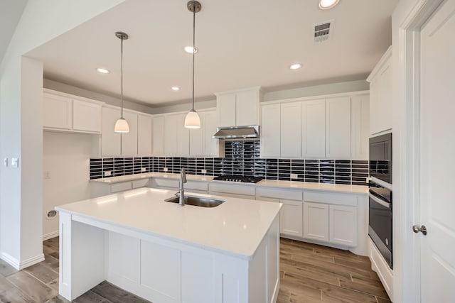 kitchen with a kitchen island with sink, hanging light fixtures, sink, white cabinetry, and light hardwood / wood-style floors