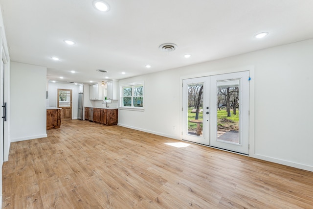 unfurnished living room featuring sink, light wood-type flooring, and french doors