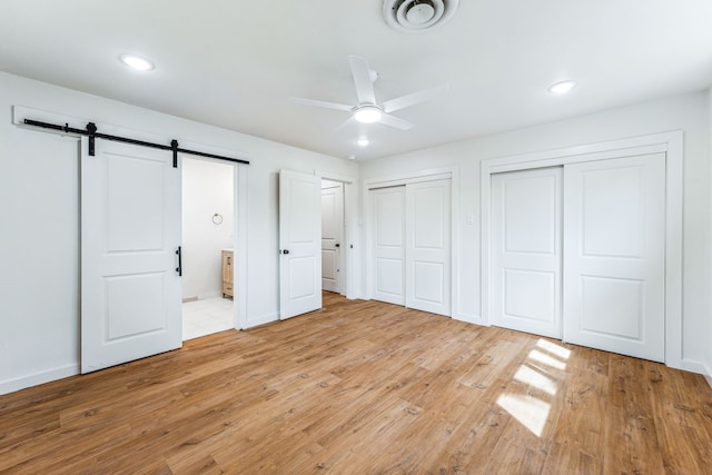 unfurnished bedroom featuring ensuite bathroom, multiple closets, a barn door, light hardwood / wood-style floors, and ceiling fan