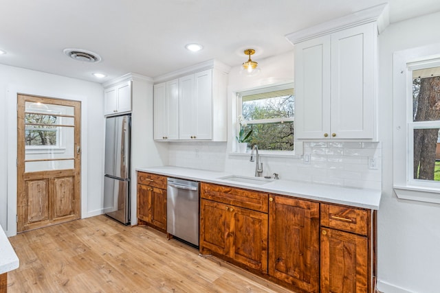 kitchen with white cabinets, light wood-type flooring, appliances with stainless steel finishes, sink, and tasteful backsplash