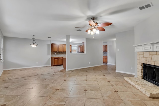 unfurnished living room with ceiling fan, light tile patterned floors, and a stone fireplace