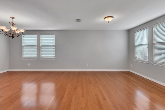 empty room featuring baseboards, light wood finished floors, a notable chandelier, and a healthy amount of sunlight