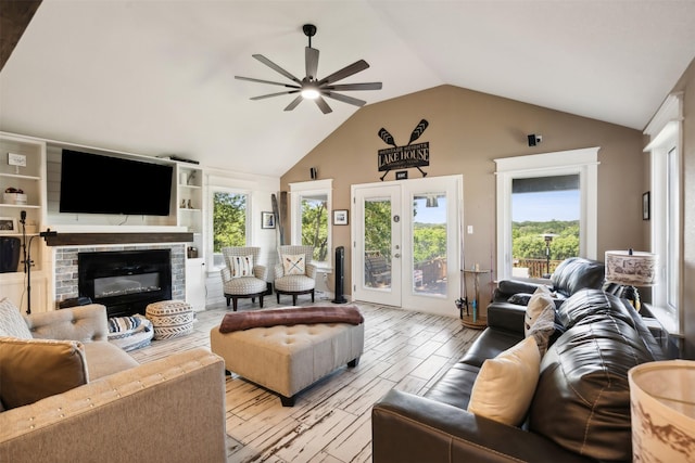 living area featuring light wood-type flooring, a glass covered fireplace, french doors, lofted ceiling, and ceiling fan