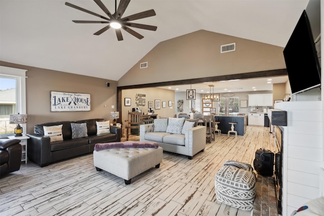 living room with visible vents, ceiling fan with notable chandelier, high vaulted ceiling, and light wood-style flooring