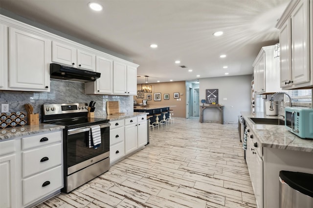 kitchen with white microwave, stainless steel range with electric cooktop, under cabinet range hood, white cabinetry, and backsplash