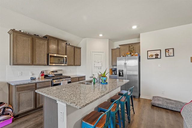 kitchen featuring a kitchen island with sink, a kitchen bar, light stone countertops, dark hardwood / wood-style floors, and appliances with stainless steel finishes