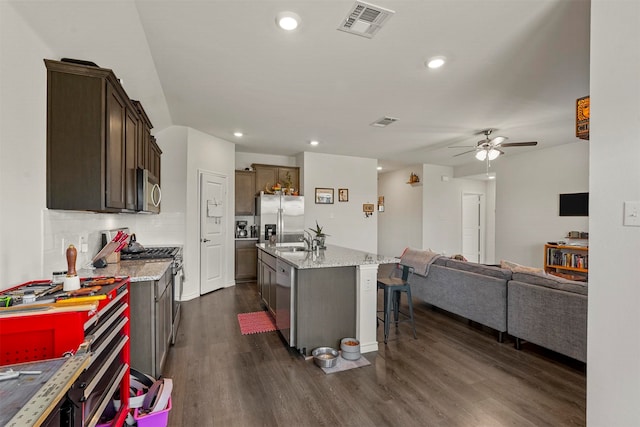 kitchen with a breakfast bar area, dark hardwood / wood-style floors, an island with sink, stainless steel appliances, and ceiling fan