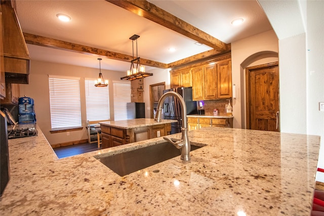 kitchen with light stone counters, sink, pendant lighting, beam ceiling, and tasteful backsplash