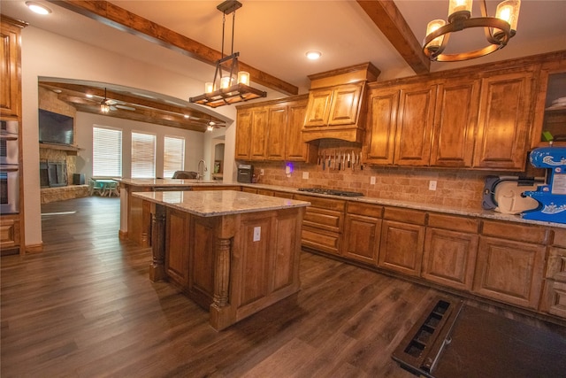 kitchen with a kitchen island, ceiling fan with notable chandelier, a fireplace, pendant lighting, and dark wood-type flooring