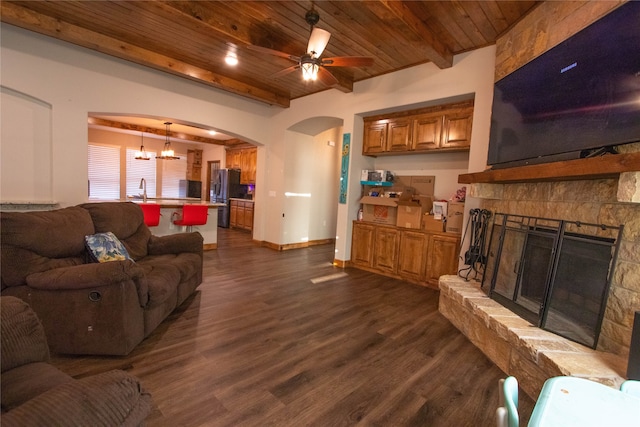 living room with ceiling fan with notable chandelier, dark hardwood / wood-style floors, wooden ceiling, and a stone fireplace