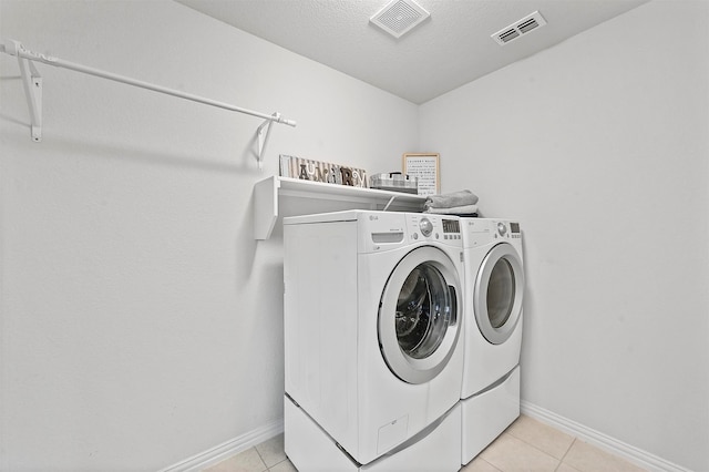 clothes washing area with a textured ceiling, washer and clothes dryer, and light tile patterned flooring