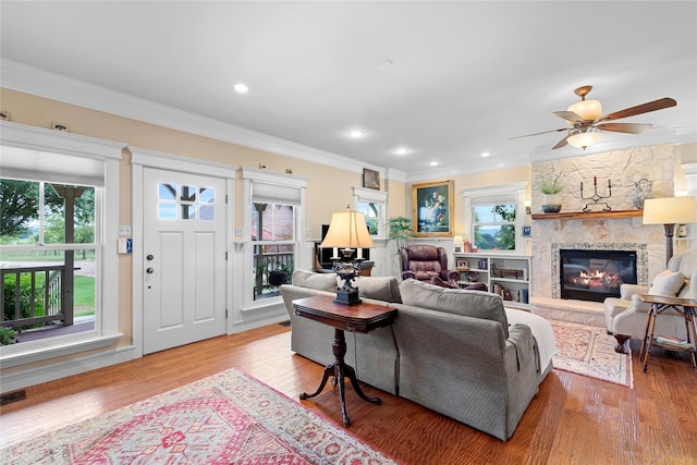 living room with crown molding, hardwood / wood-style flooring, ceiling fan, and a stone fireplace