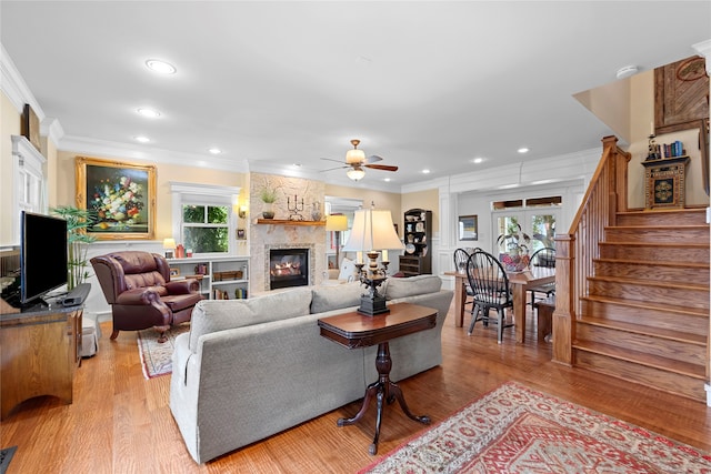 living room with crown molding, light hardwood / wood-style flooring, ceiling fan, and a stone fireplace