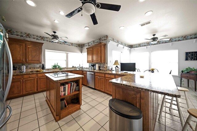 kitchen with light tile patterned floors, kitchen peninsula, a center island, ceiling fan, and appliances with stainless steel finishes