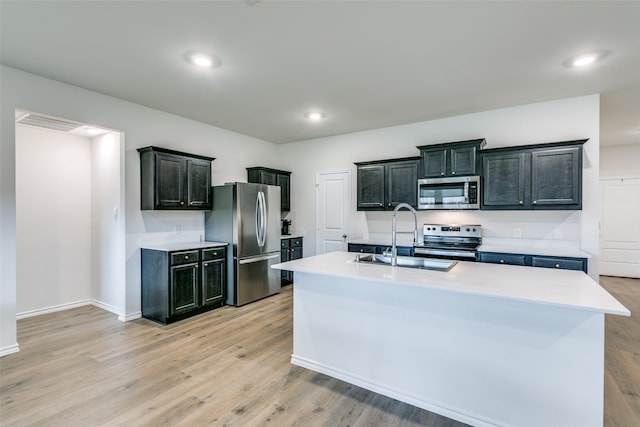 kitchen with an island with sink, appliances with stainless steel finishes, sink, and light hardwood / wood-style flooring