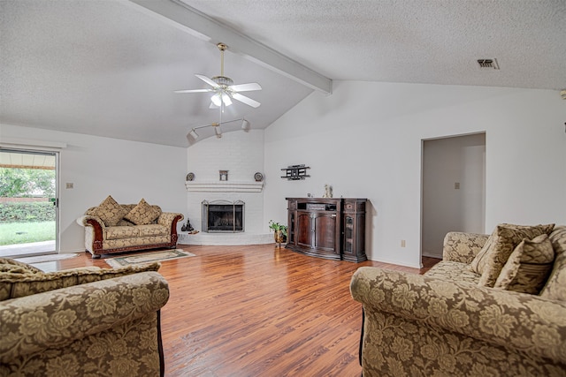 living room with a fireplace, a textured ceiling, ceiling fan, lofted ceiling with beams, and hardwood / wood-style flooring