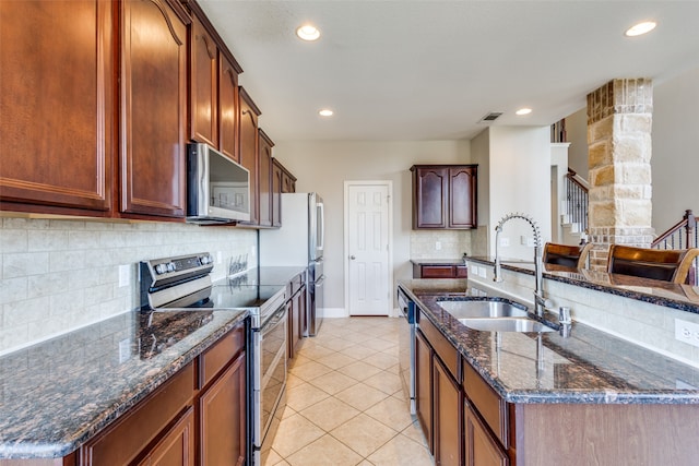 kitchen with light tile patterned floors, appliances with stainless steel finishes, sink, decorative backsplash, and dark stone countertops