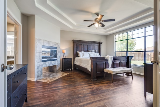 bedroom with a tiled fireplace, a tray ceiling, ceiling fan, and dark hardwood / wood-style floors