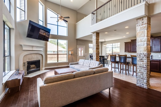 8521 Bonanza St, Aubrey, TX 76227 - living room featuring ornate columns, ceiling fan, a towering ceiling, dark wood-style flooring, and a tiled fireplace