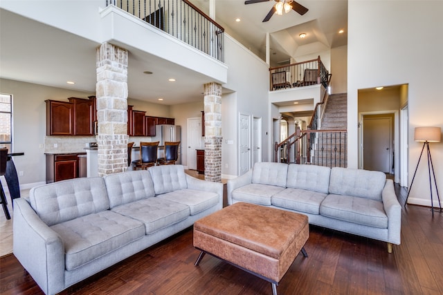 living room with a towering ceiling, dark wood-type flooring, ceiling fan, and decorative columns