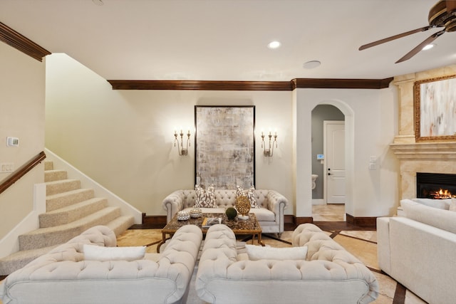 living room featuring a premium fireplace, ornamental molding, and ceiling fan