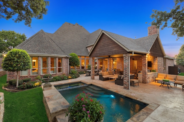 back of house with an outdoor living space with a fireplace, a patio, a shingled roof, brick siding, and a chimney