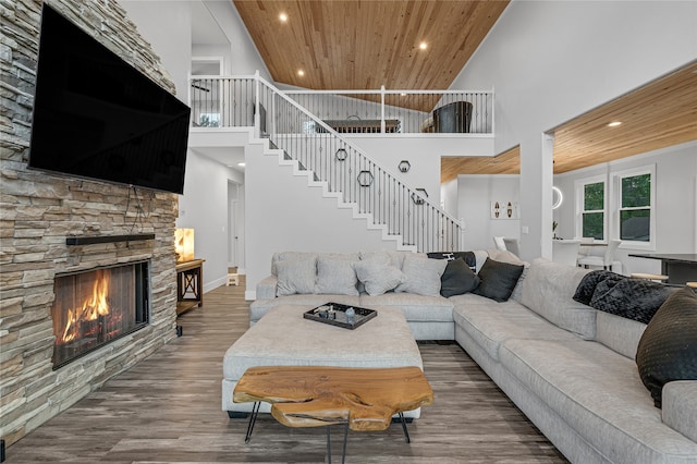 living room featuring a towering ceiling, wood ceiling, wood-type flooring, and a stone fireplace