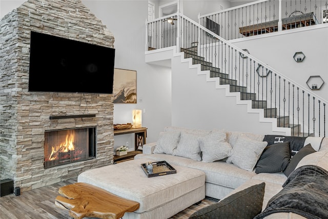 living room featuring a high ceiling, wood-type flooring, and a stone fireplace