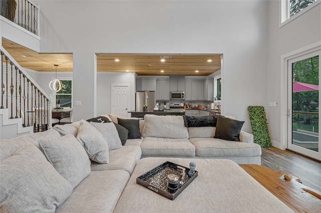 living room with a towering ceiling, wood-type flooring, wood ceiling, and a healthy amount of sunlight