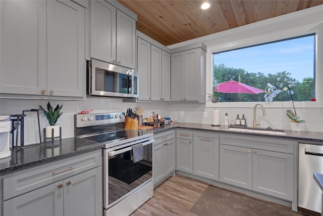 kitchen with light wood-type flooring, dark stone counters, wood ceiling, sink, and appliances with stainless steel finishes