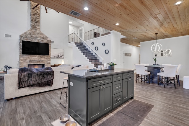 kitchen with a kitchen island, gray cabinetry, wooden ceiling, a stone fireplace, and hanging light fixtures