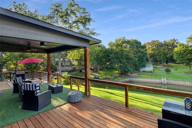 wooden terrace featuring ceiling fan, a lawn, and a water view