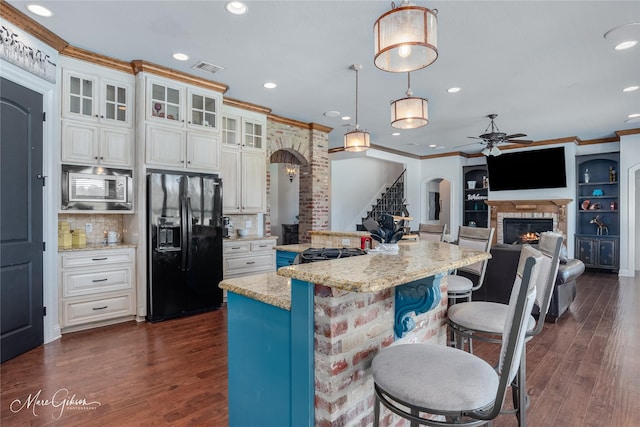 kitchen featuring light stone countertops, black refrigerator with ice dispenser, decorative backsplash, hanging light fixtures, and stainless steel microwave