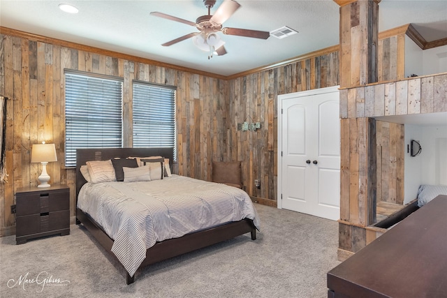 carpeted bedroom with ceiling fan, ornamental molding, and wooden walls