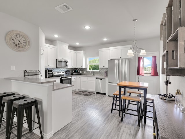 kitchen featuring decorative light fixtures, light hardwood / wood-style floors, stainless steel appliances, sink, and white cabinets